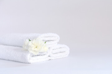 Three white neatly folded terry towels with a jasmine flower on a light background.