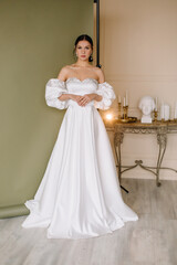 Young brunette woman stands in a white wedding dress on a green background