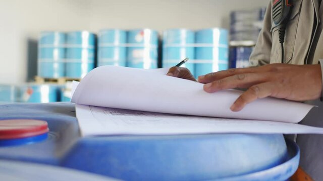 An employee holding a clipboard examining something in an industrial plant and recording the results on a paper sheet.