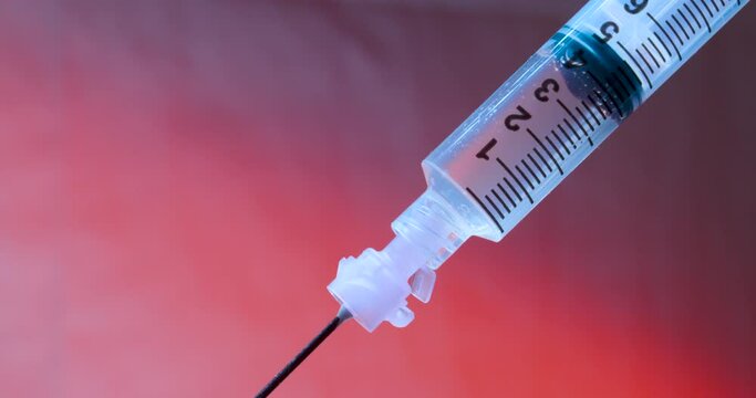 Diagonal Syringe Plunger Pushing Liquid Through Barrel In Blue Light On Red BG