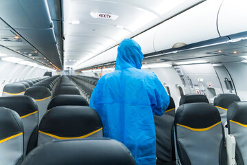 Airline staffs in protective suit (PPE) wearing medical face mask disinfecting spray for covid-19 at airplane cabin to disease prevention.