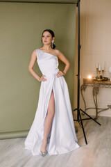 Fototapeta premium Young brunette woman stands in a white wedding dress on a green background