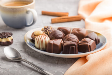 Different chocolate candies and a cup of coffee on a gray concrete background. side view, selective focus.