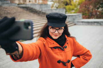 Obraz premium Young woman wearing a coat and hat takes a photo of herself