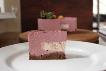 A piece of homemade mousse sweet pink cake on the plate. The concept of proper nutrition. A piece of cake on the foregraund and a cake blurred on the background.