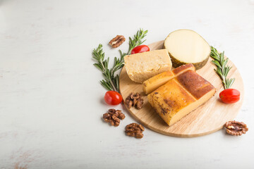 Smoked cheese and various types of cheese with rosemary and tomatoes on wooden board on a white background. Side view, copy space.