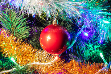 Decorated Christmas tree closeup shot. Red ball in the middle, illuminated garland with blue, orange, green lights. White and golden tinsel. New Years, winter holiday light decoration