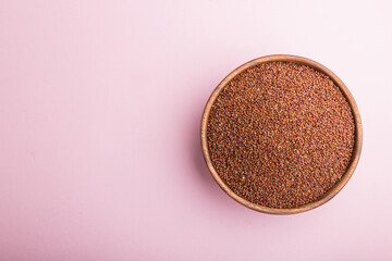 Wooden bowl with raw red quinoa seeds on a pastel pink background.  Top view, copy space.