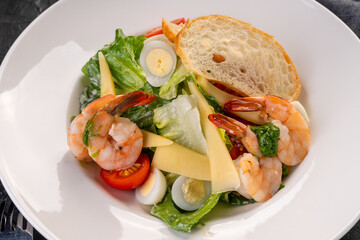 salad with tiger shrimps(prawns) in a white plate on a dark background. Caesar Salad with seafood
