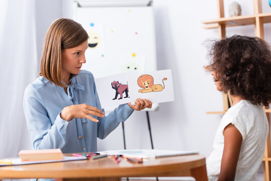 Psychologist showing pictures with animals to african american girl with blurred coffee table foreground in office