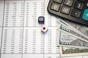 On a document with columns of numbers, there are dice next to dollars and a calculator.