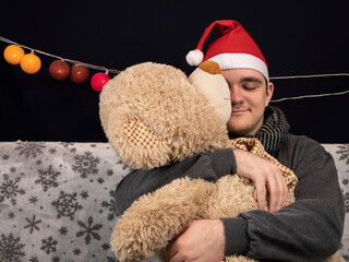 a young guy sits on the couch and hugs a teddy bear