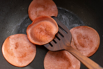 closeup frying pork bologna in black pan with small amount of cooking oil © Thitiporn