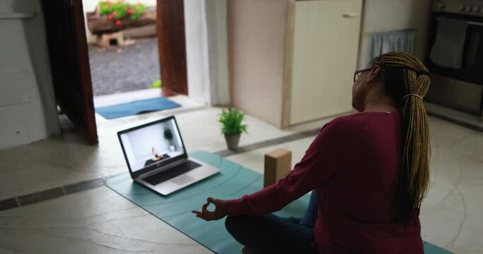 African senior woman doing online yoga lesson at home during coronavirus outbreak - Old female person meditating using computer laptop - Technology and zen concept 