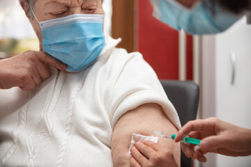 senior adult elderly woman with grey hair is receiving a vaccination against covid
