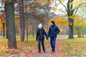teen girl and boy walking through the park and enjoys autumn, beautiful nature with yellow leaves
