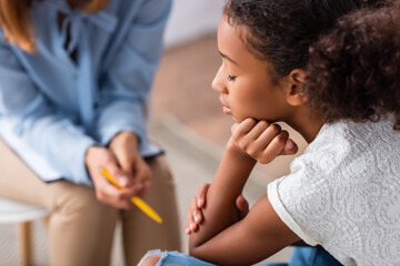Close up of upset african american girl with closed eye near psychologist during consultation on blurred background