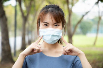 Asian woman pointing and recommending the use of face mask, concept of taking precaution measure, social distancing, new normal lifestyle while waiting for coronavirus cure, COVID-19 vaccine