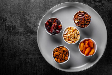 almonds, peanuts, walnuts, dates, dried apricots in a plate on Dark grey black slate background