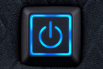 Macro shot of a plastic button with a blue power symbol, sewn into modern clothing, top view.