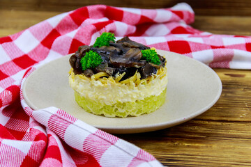 Tasty layered salad with roasted mushrooms, potato, eggs, cheese and mayonnaise on wooden table