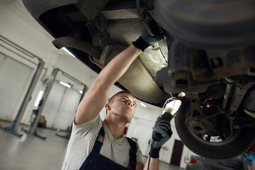 Mechanic working with flashlight under machine bottom