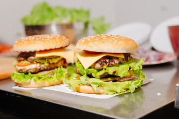Two large burgers on the kitchen table in the cafe kitchen. Double burgers with cheese and fresh salad
