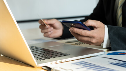 Mobile phones, online payments, Ik side holds credit cards and uses smart phones to shop online and laptop with graphs on the table.