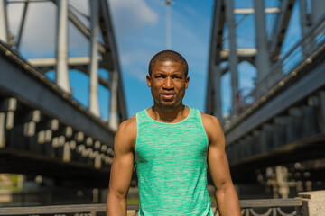 Waist up portrait of confident Black male runner standing on bridge and looking at camera while resting after sports training