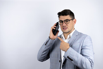 Business young man wearing a casual shirt over white background smiling, pointing to the phone that he has in his ear