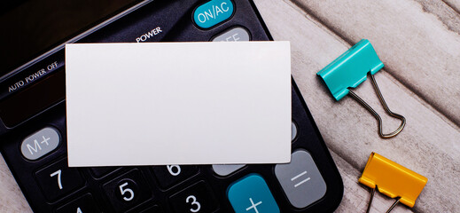 Stationery concept. Calculator, multi-colored paper clips and a white blank card on a light wooden...