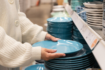Woman customer choosing and buying blue clay dishes plates, dinner utensil for her kitchen in...