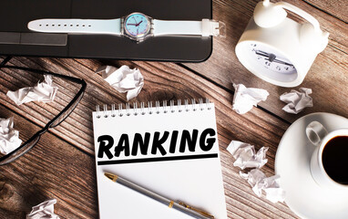 There is a cup of coffee on a wooden table, a clock, glasses and a notebook with the word RANKING....