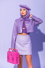 young woman dressed in doll style posing with pink retro tape recorder on violet colorful background