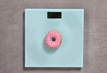 Weight scale with sweet pink glazed doughnut with sprinkles top view, copy space for text or design, sugar, junk food concept background