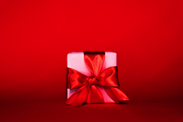 Romantic surprise. Valentine Day. Pink wrapped gift box with ribbon bow isolated on red empty space festive background. Holiday greeting. Anniversary present.