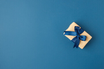 Paper craft gift box with stylish bow on blue background with copy space. Greeting card concept....