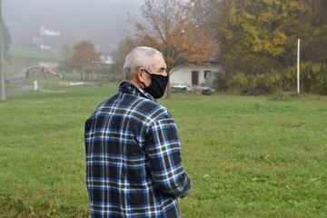 An older man with a covid19 mask on his face in the village with a facial expression 