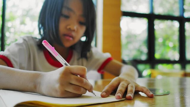 A six-year-old Asian girl is doing homework in the living room.