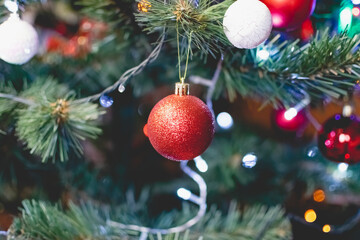 Bright red Christmas toys on the branches of an artificial Christmas tree. Snow balls and berries. A variety of festive accessories shimmer next to colored garlands and lanterns