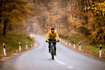 Fototapeta premium Young man biking on a country road through autumn forest