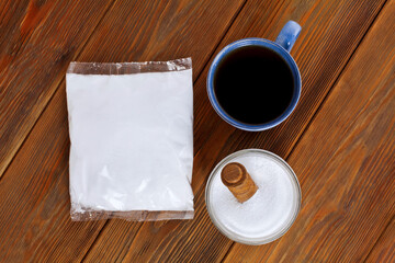 Fructose in a transparent pack with cup of tea, glass jar and wooden scoop of sorbitol on a wooden background. Different sweeteners concept. Top view.