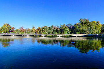 Landscape with long old grey bridge and many large green trees near the lake in Carol Park in...