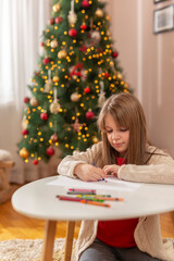 Little girl drawing by the Christmas tree