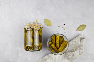Pickled cucumbers in a glass jar and bowl on a light background.  Homemade fermented or marinated...