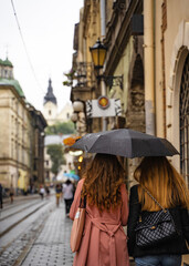 two young woman are walking with umbrella in old European city under the rain