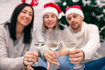 Young happy couple in Christmas hats near a Christmas tree kissing, holding glasses of wine. New Year celebration
