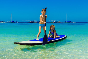 Smiling little girl and boy having fun on a paddleboard in the tropical sea. The concept of travel and family holidays.