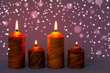 Natural beeswax candles with flame on bright shiny purple background. Decoration with copy space.