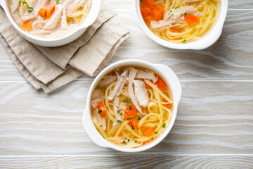 Warm healthy homemade chicken soup in white ceramic bowls on white wooden table background. Traditional tasty chicken soup great for health and immune system. Top view